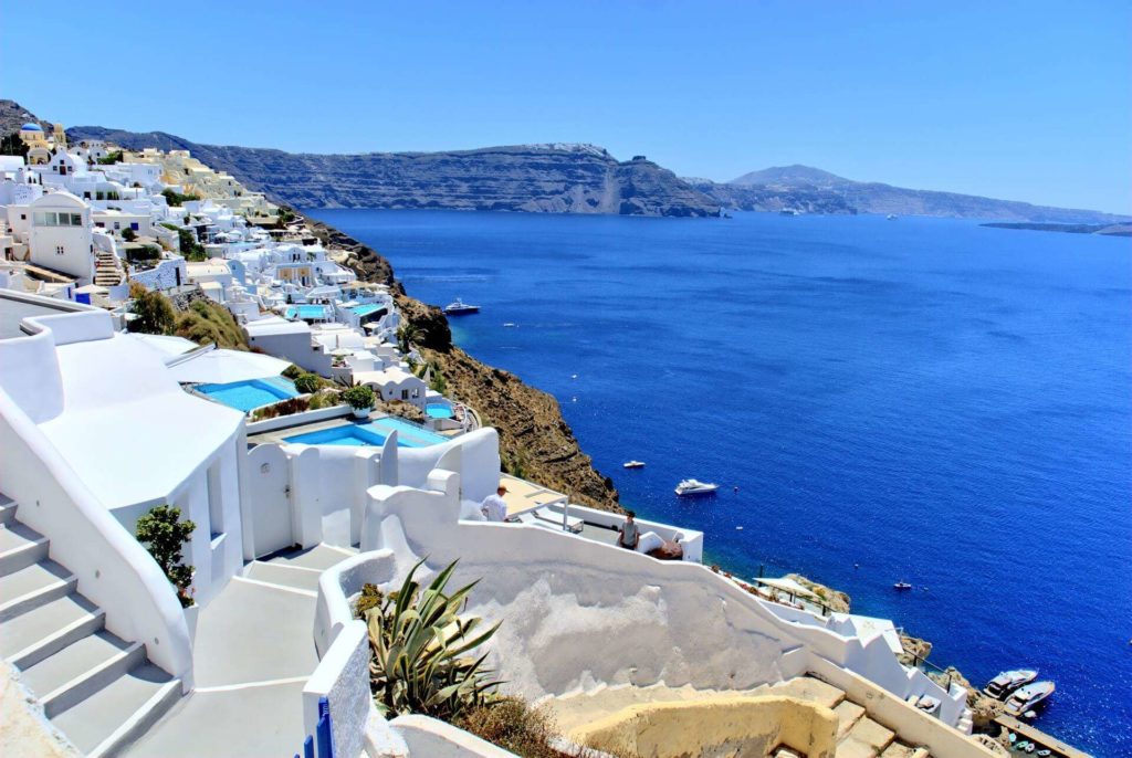 Santorini's white houses on the rocks with small pools, and beautifull sea in the back.