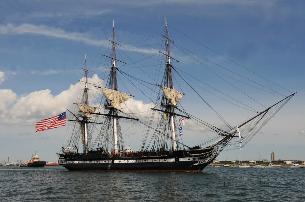 Picture of the USS Constitution on water, American flag waving from behind